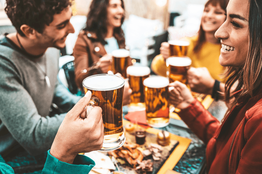 A group of friends toasting with beer mugs at a lively outdoor gathering.