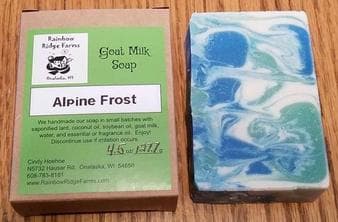 A bar of Alpine Frost goat milk soap beside its packaging, featuring blue and white swirls.
