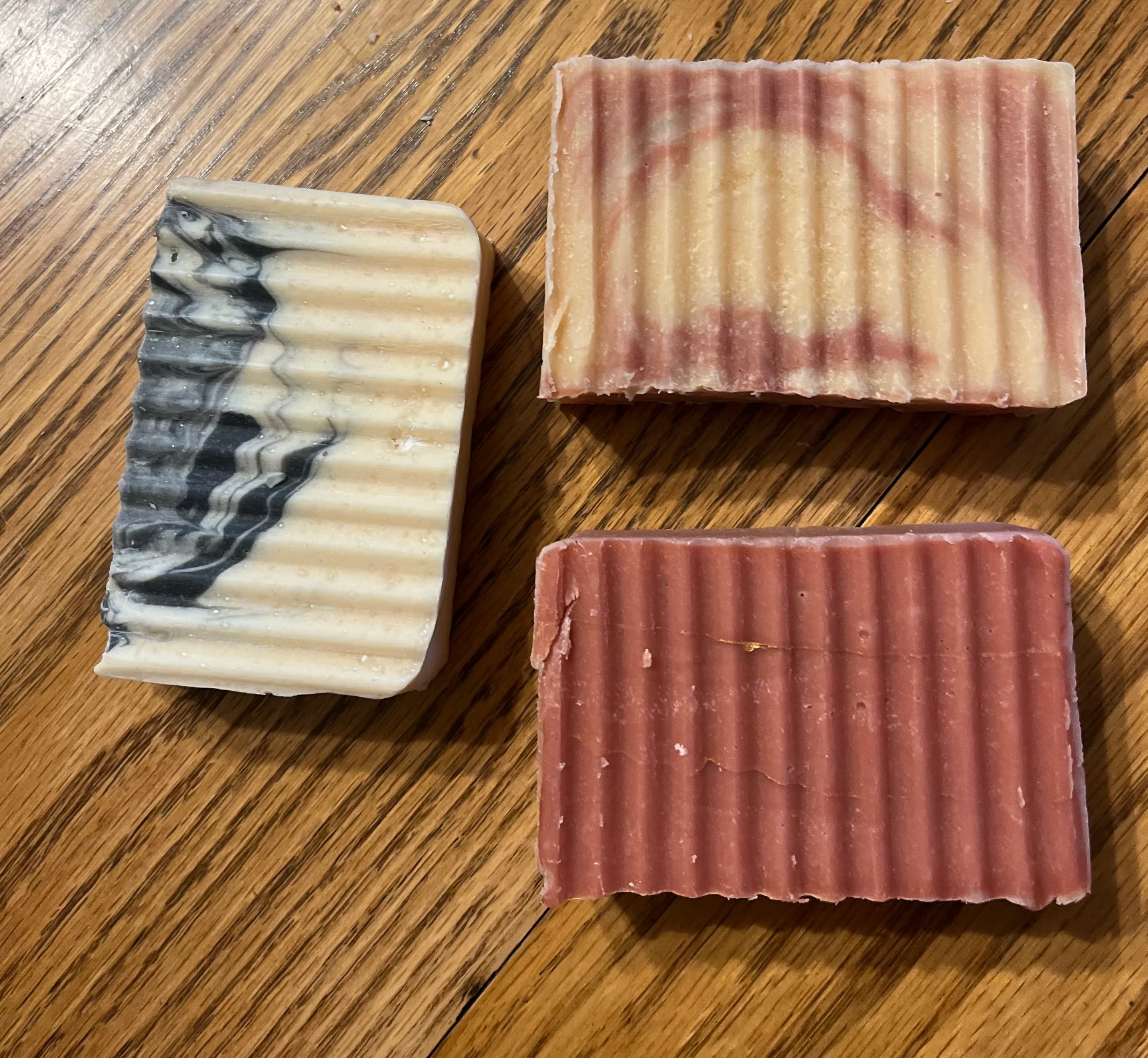 Three bars of textured soap in different colors on a wooden surface.