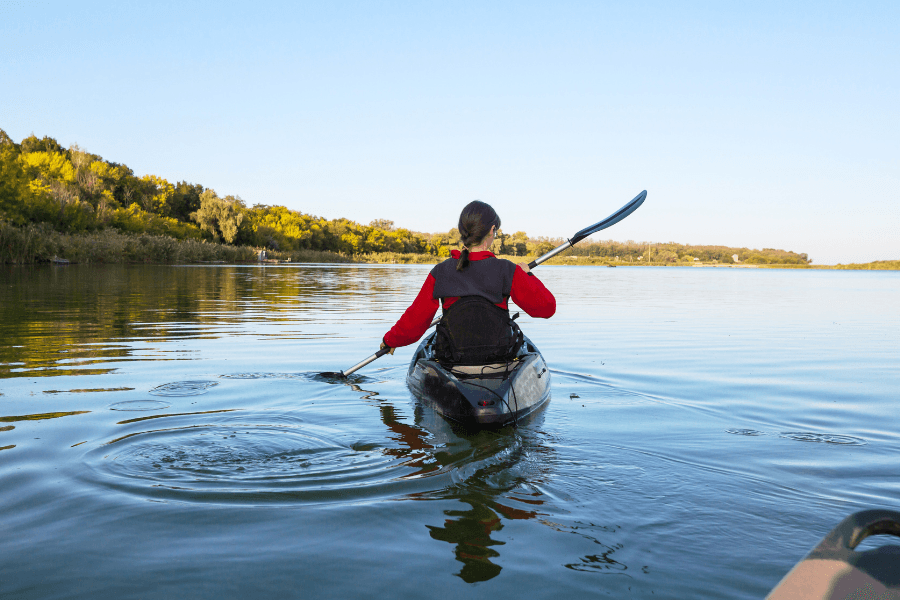 A person in a kayak paddles through a calm lake surrounded by greenery.