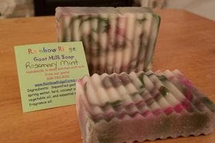 Two bars of rosemary mint goat milk soap beside a business card on a wooden surface.