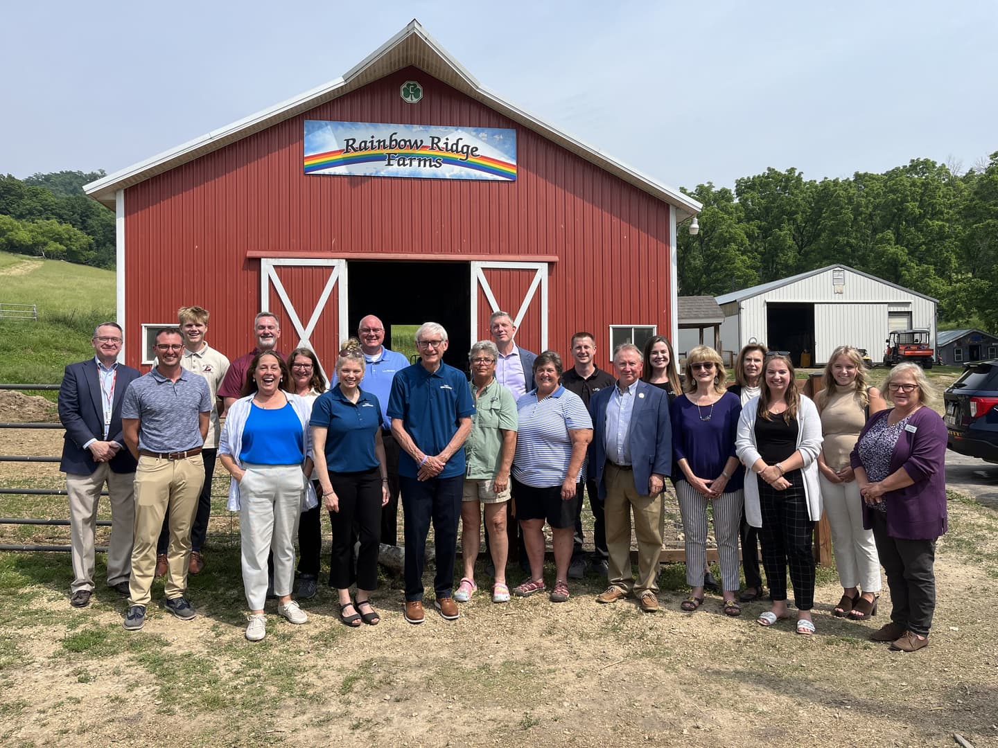 Group of people posing in front of a red barn with a sign that reads "Rainbow Ridge Farms."