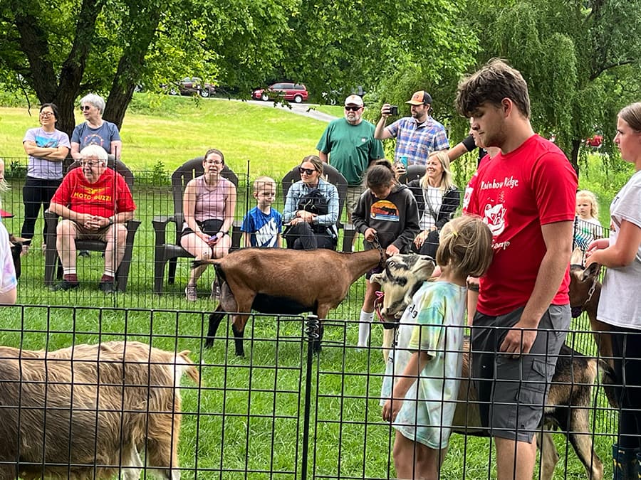 A group of children and adults watch as goats interact during a farm event.