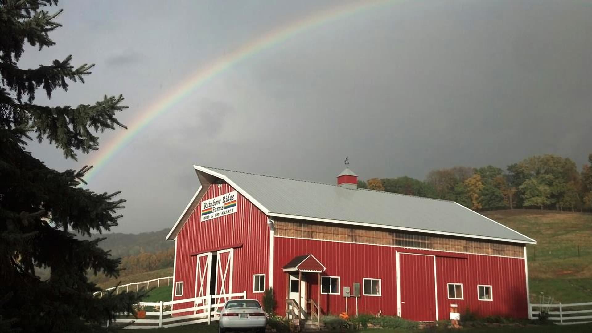 A red barn with a sign reading "Rainbow Ride Farms" is set against a backdrop of a rainbow and trees.